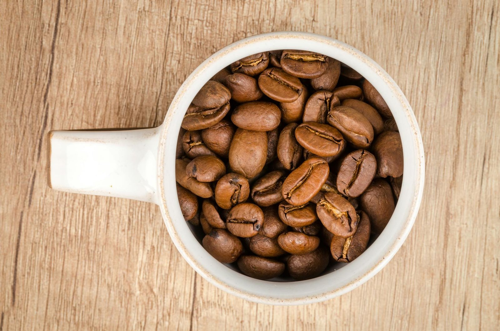 roasted coffee beans inside white ceramic mug cup of coffee